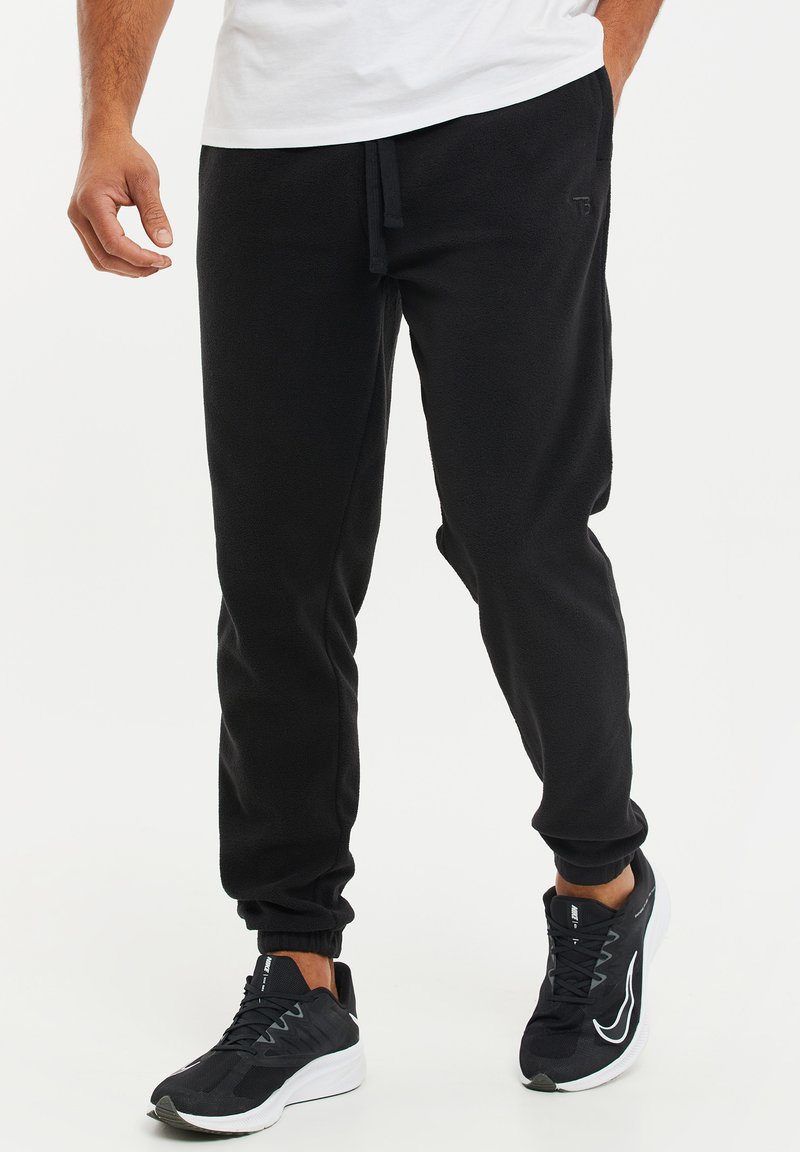 Zwarte fleece jogger broek met een trekkoord in de taille, fitted boorden en een subtiel logo detail op de dij. Gecombineerd met zwarte sportschoenen.
