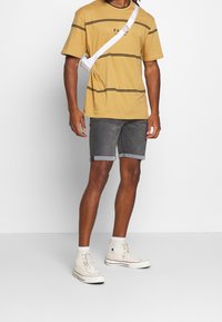 Geel T-shirt met korte mouwen en zwarte strepen, grijze denim shorts met opgerolde boorden, en witte hoge sneakers. Witte schoudertas.