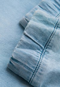 Světle modrá denimová látka s detailním záběrem na složený manžetu se shromážděnou texturou a viditelnými stehy.