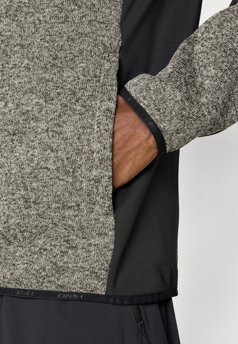 Szara i czarna sportowa kurtka z mieszanką dzianiny i gładkich tekstur, z boczną kieszenią i wyraźnymi detalami szwów.