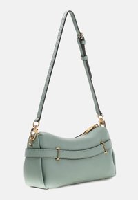 Miętowo zielona skórzana torba na ramię o zakrzywionym kształcie, ze złotymi ozdobami i odpinanym paskiem. Teksturowana powierzchnia z zamkiem błyskawicznym.