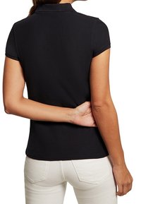 Polo noir à manches courtes avec col, texture lisse et silhouette ajustée, vu de dos porté avec un pantalon clair.