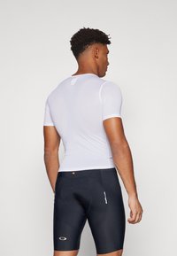 Haut blanc à manches courtes, ajusté, avec un motif texturé, associé à un short de cyclisme noir avec un détail de couture en forme de cœur et un logo.