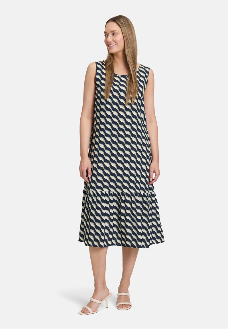 Granatowa i kremowa bezrękawnikowa sukienka w faliste wzory z falbaną u dołu. Gładki materiał, sylwetka w kształcie litery A, długość do kolan.