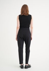 Top sans manches noir et pantalon noir ajusté, présentant une coupe slim et une longueur cheville. Tissu lisse avec un minimum de détails.