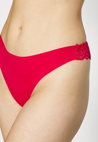 Rode bikini onderkant met een gladde stof en kanten accenten langs de taille. Het ontwerp is minimalistisch met een lage snit.