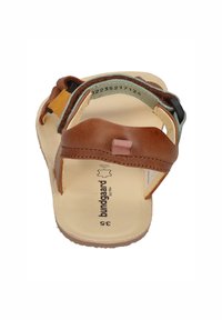 Braune Ledersandalen mit verstellbaren Riemen, hellbraunem Fußbett und flacher Sohle. Mit einem rosa Akzent und dem Markenlogo auf der Innensohle.