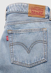 Ανοιχτό μπλε τζιν παντελόνι με χαρακτηριστική ταμπέλα από καφέ δέρμα, που φέρει κόκκινο λογότυπο και χαρακτηριστική ραφή arcuate στην πίσω τσέπη.