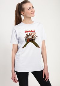 Žena v bílém tričku s motivem "School of Rock", na kterém je muž hrající na kytaru a děti v školních uniformách za ním.