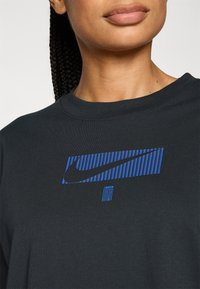 Nike black t-shirt featuring a blue graphical logo with vertical stripes. The fabric is smooth with a crew neckline and short sleeves.