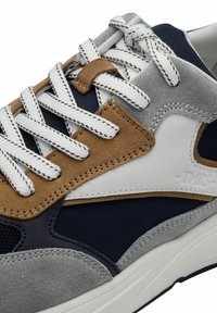 Sneaker z szarym zamszem, granatową siateczką i brązowymi skórzanymi akcentami. Białe sznurówki i przeszycia. Okrągły czubek z gumową podeszwą.