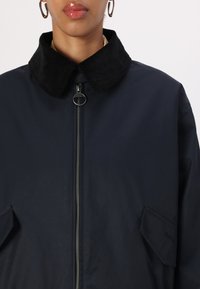 Navy jacket featuring a corduroy collar, front zip closure, and two side pockets with a smooth outer texture. Simple, functional design.