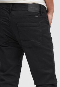 Črne kavbojke iz jeansa z klasičnim krojem, zadnjimi žepi z nežnimi detajli šivanja in etiketo znamke na pasu.