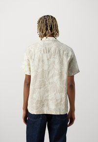 Korte mouwen, lichtromige blouse met knopen en een bloemenpatroon. Gemaakt van textuurstof. Heeft een rechte zoom en details bij de schoudernaad aan de achterkant.