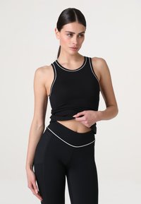 Top nero senza maniche con bordature bianche, design aderente, materiale elasticizzato. Abbinato a leggings neri a vita alta, con una fascia in vita liscia.