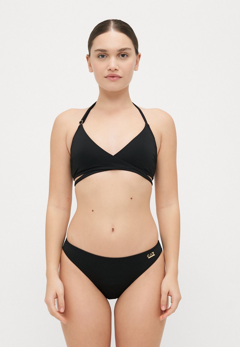 Melna bikini komplekts, kas ietver apmetuma stila topu ar regulējamām siksnām un zelta detaļām, kas sasaistīts ar atbilstošām zemas jostasvietas biksītēm. Gluda tekstūra.