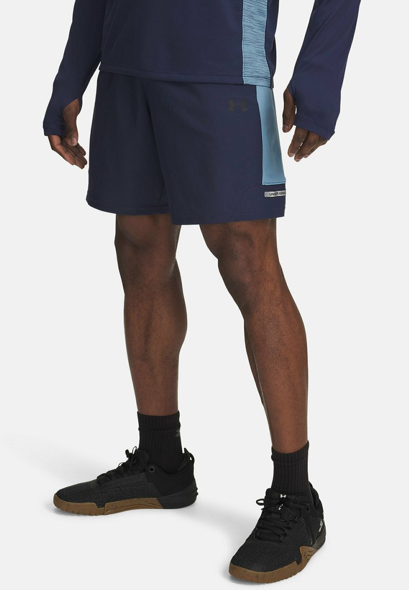 Marineblauwe sportshorts met een lichtblauwe zijpaneel, vochtafvoerende stof, gecombineerd met zwarte gestructureerde sneakers en zwarte crew-sokken.