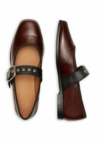 Zapatos Mary Jane de cuero marrón con una correa negra y hebilla. Presentan una textura suave, punta cuadrada y suela plana. Diseño minimalista.
