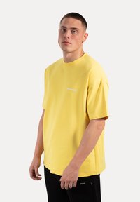 Żółta krótko rękawowa koszulka z bawełny, z okrągłym dekoltem i białym haftem "Smallbox Sport" na piersi.