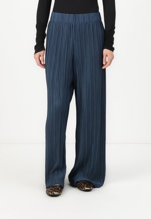 Pantalons larges plissés navy avec une taille élastique, en matériau texturé. Portés avec des chaussures imprimé animal.
