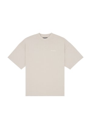 Femme aux cheveux bouclés portant un t-shirt beige oversize, un short rayé pastel et des bottes en cuir noires montantes jusqu'aux genoux, debout devant un fond uni.