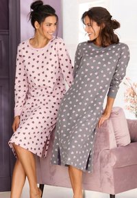 Two women wearing long-sleeved nightgowns. One is light pink with dark purple hearts; the other is gray with light pink hearts. Both have side slits.