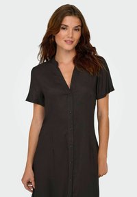 Robe noire à manches courtes avec un col et une patte de boutonnage. Présente une coupe ajustée avec une texture subtile et une finition en tissu lisse.