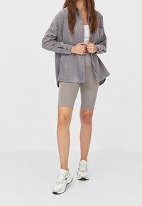 Grå manchester skjorta med knappar och uppkavlade ärmar, kombinerad med ljusgrå cykelshorts och vita sneakers med metallicdetaljer.