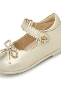 Zapato Mary Jane metálico dorado con detalle de lazo y correa ajustable, que presenta una textura lisa y un diseño de punta redondeada.
