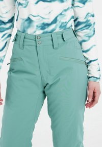 Mint zelene skijaške hlače izrađene od mekog, vremenski otporog materijala; imaju visoki pojas, dva džepa sa patentnim zatvaračem i detalj s gumbom.