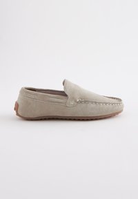 Mocassin en daim beige clair avec couture style mocassin et semelle en caoutchouc marron, présenté de profil sur fond blanc.