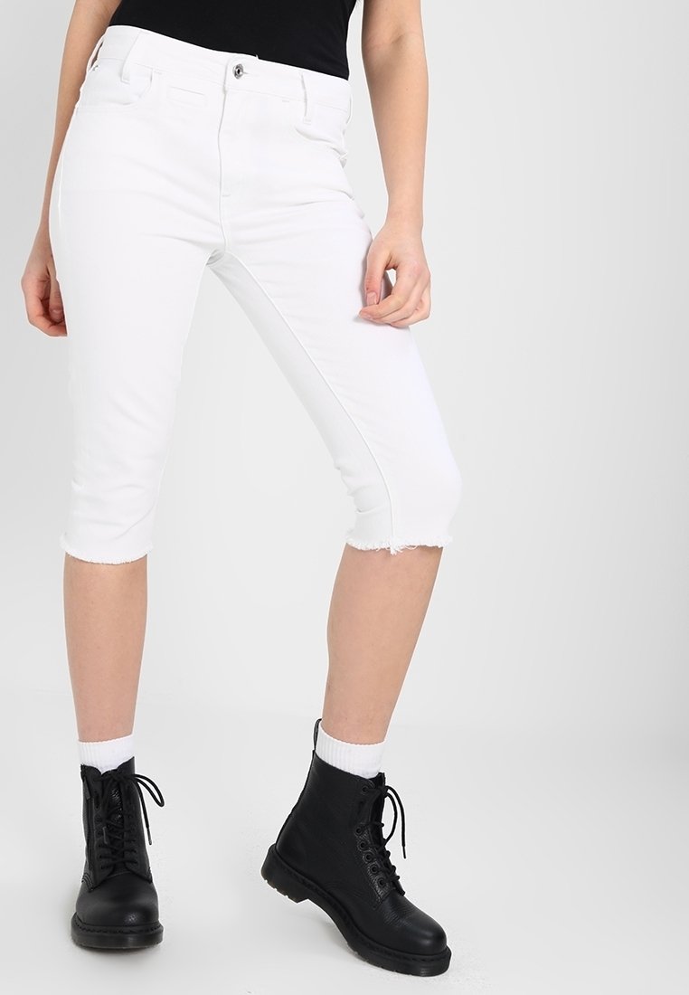 Valkoiset lyhyet farkut, joissa on risat helmat, valmistettu denimistä, yhdistetty mustiin nauhakiinnitteisiin saappaisiin ja valkoisiin crew-sukkiin. Yksinkertainen muotoilu, kapea malli.