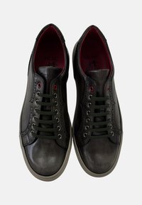 Zapatillas de cuero negro con cordones verdes, forro interior rojo y detalles perforados. Presentan una puntera redondeada y suela de goma.