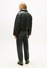 Giacca a vento nera con colletto alto, vestibilità rilassata ed elastico in fondo. Abbinata a jeans grigio scuro e sneakers con dettagli verdi.