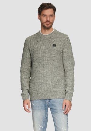 Grauer Strickpullover mit geripptem Muster, Rundhalsausschnitt und kleinem schwarzen Logo auf der Brust, kombiniert mit hellblauen, verwaschenen Jeans.