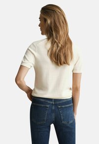 Cremfarbener Kurzarm-Oberteil aus weichem Stoff, kombiniert mit dunkelblauen, eng anliegenden Jeans mit zwei Gesäßtaschen und klassischem Schnitt.