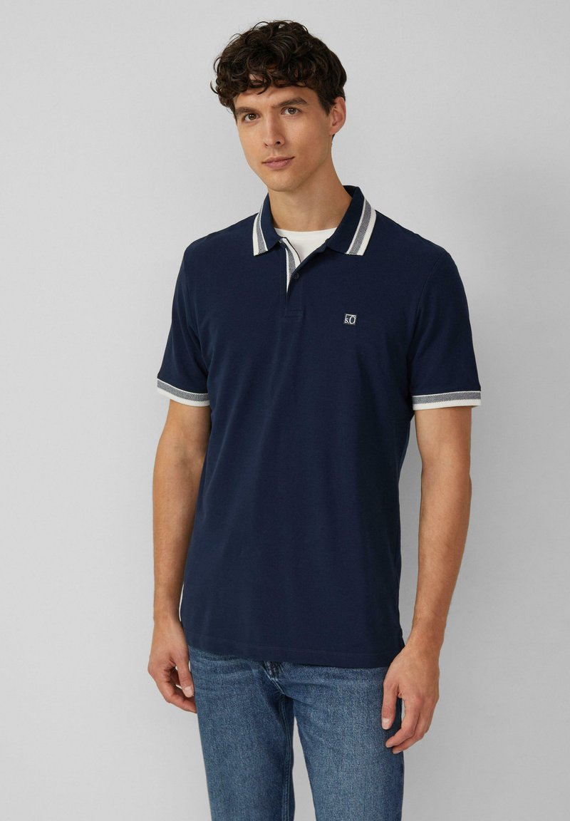Marineblauwe poloshirt met gestreepte kraag en manchetten, gemaakt van een gladde stof. Voorzien van een klein logo op de borst en een klassieke pasvorm.
