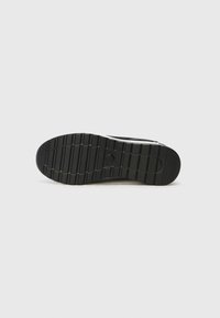 Black rubber shoe sole with a textured pattern of horizontal and vertical grooves and a round logo detail in the center.