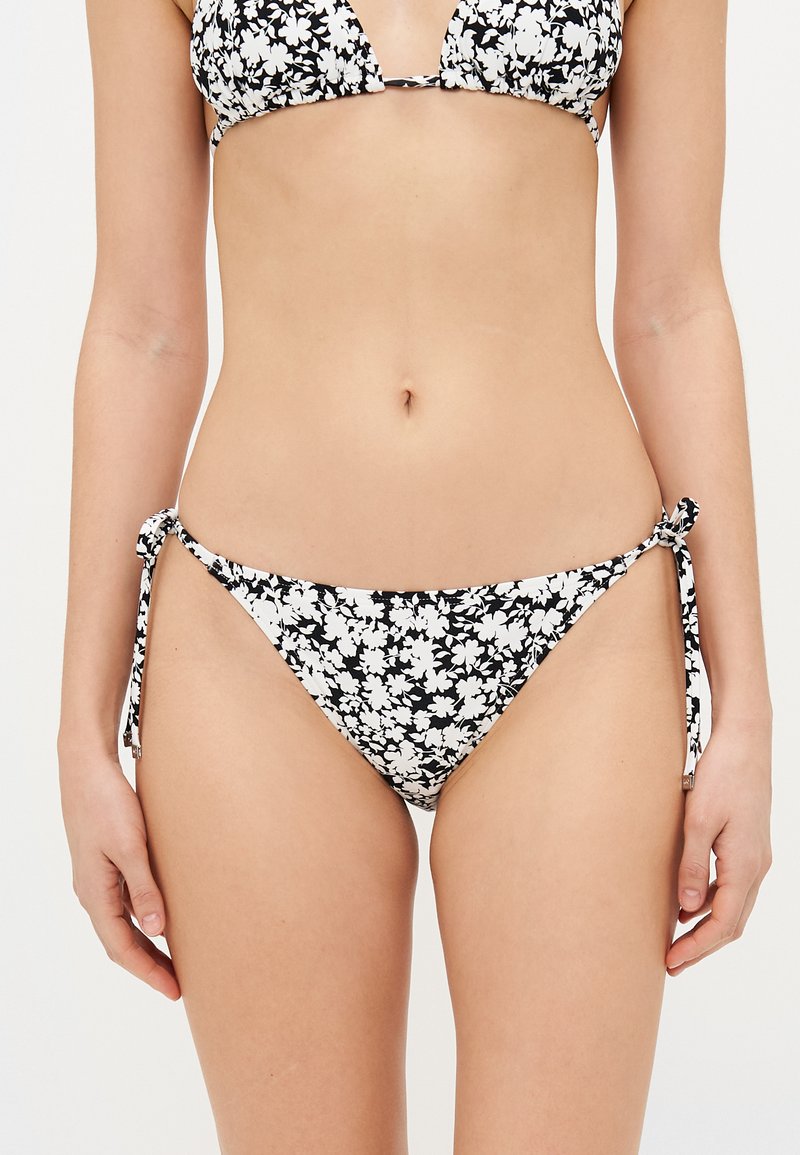 Svart och vit blommig bikini med triangulär topp och botten med knytförslutningar i sidan. Tyget är slätt med en glansig finish.