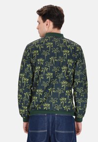 Groene bomberjack met een gele palmboomprint, geribbelde manchetten en zoom, en een soepele textuur. Geschikt voor casual kleding.