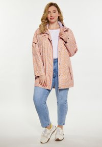 Lahka roza dežna jakna z vzorcem leoparda, ki ima visok ovratnik, gumbke na zapenjanje in zadrgo na stranskih žepih. Nosijo jo preko modrih kavbojk in superg.