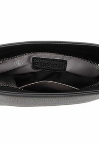 Bolso de cuero negro con un exterior texturizado, cierre de cremallera, forrado en satén gris, con un pequeño bolsillo interior que lleva una etiqueta de logo.