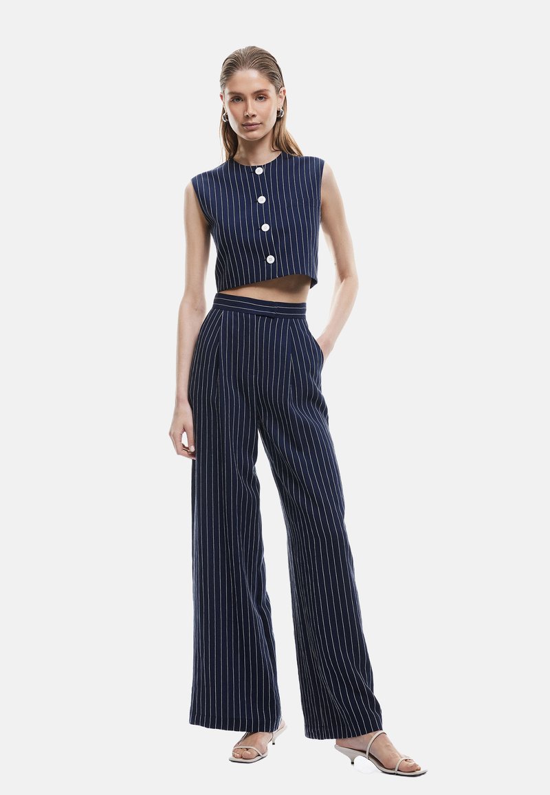 Crop top rayé bleu marine avec des boutons ronds associé à un pantalon taille haute à jambes larges. Présente des lignes épurées et un tissu à texture lisse.