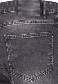 Jeans en denim noir avec une étiquette en cuir, comportant cinq poches, une texture délavée et des coutures blanches contrastantes le long des coutures.