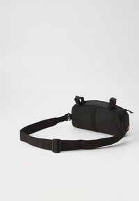 Black nylon waist bag with a cylindrical shape. Features an adjustable strap and two buckles. Textured surface and zippered compartment.