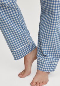 Pantaloni del pigiama a quadri blu e bianchi con taglio dritto, caratterizzati da un bordo bianco sul fondo e pelle visibile alle caviglie.