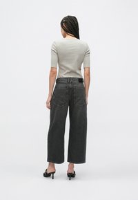 Světlé šedé přiléhavé tričko s krátkými rukávy v kombinaci s tmavě šedými džíny s širokými nohavicemi. Džíny mají dvě zadní kapsy a pas ve střední výšce.