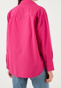 Camicia a maniche lunghe rosa brillante con colletto a punta, polsini con bottone e vestibilità comoda, realizzata in tessuto liscio e con orlo leggermente curvo.