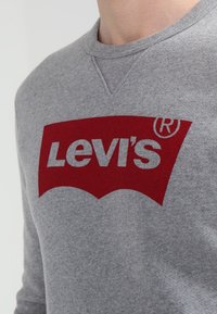 Sweat-shirt gris en mélange de coton avec un logo Levi's rouge en forme d'arche audacieuse. Dispose d'un col rond et de poignets côtelés.