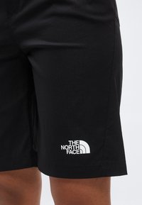 Κοντινό πλάνο μαύρων σορτς που φοριούνται σε πόδι, με το λογότυπο "The North Face" σε λευκό στο κάτω μέρος της αριστερής πλευράς του ποδιού.